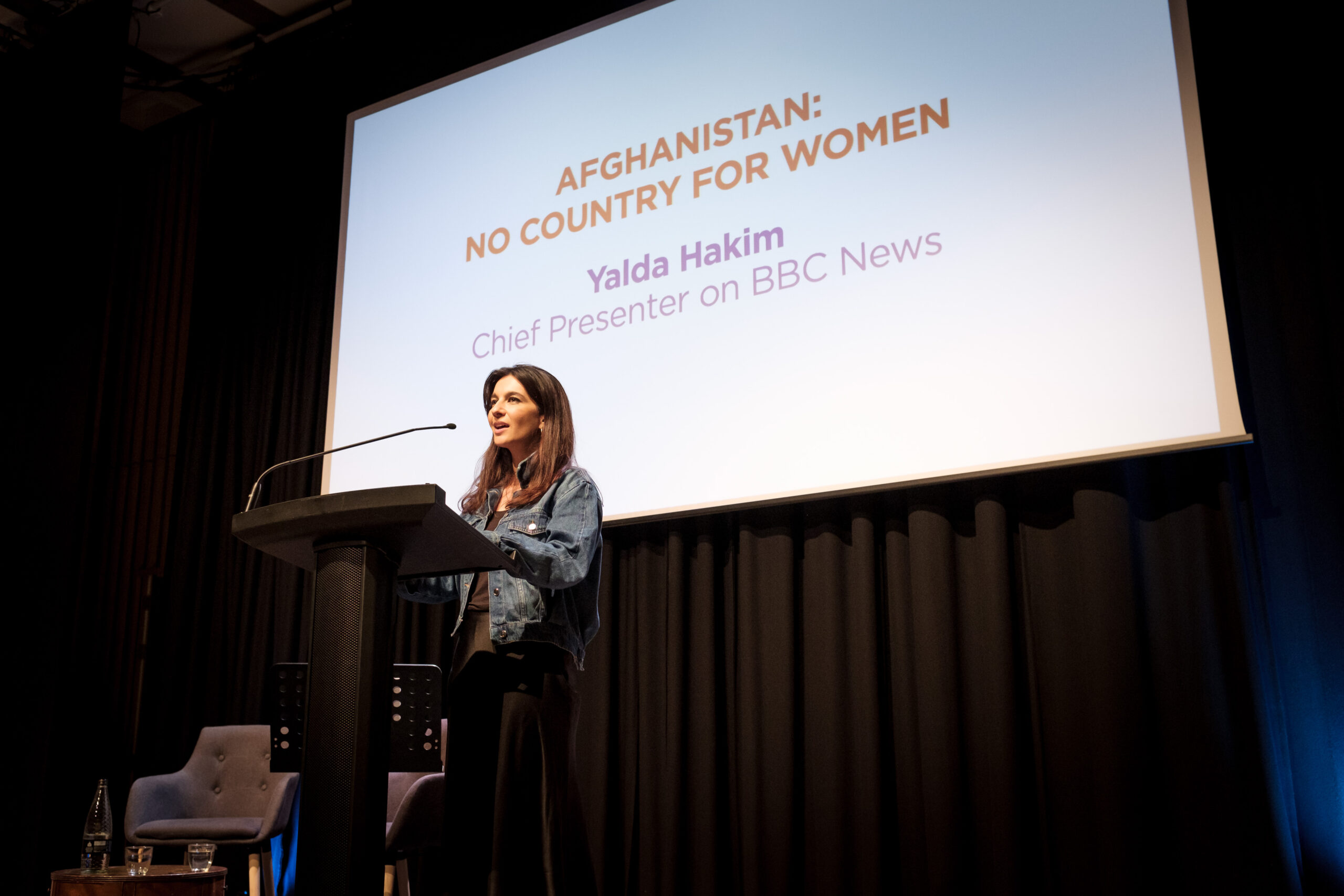 BBC presenter Yalda Hakim presents at the HIAS+JCORE launch event. She is standing at a lectern in front of a presentation titled: 'Afghanistan: No country for women.'